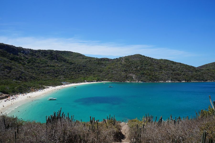 Praia do Forno in Arraial do Cabo seen from the hillside: a curve of white sand and turquoise water below green hills