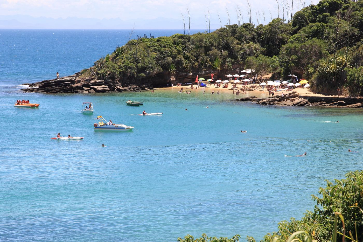A small cove with a sandy beach, rocks and boats on clear blue water at Praia da Azedinha in Búzios