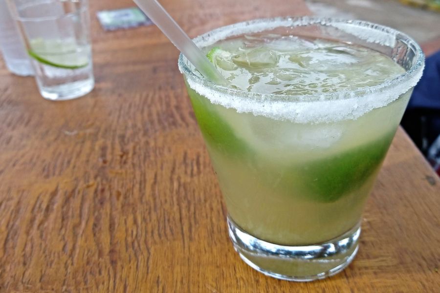 A lime caipirinha with crushed ice and a straw on a wooden table