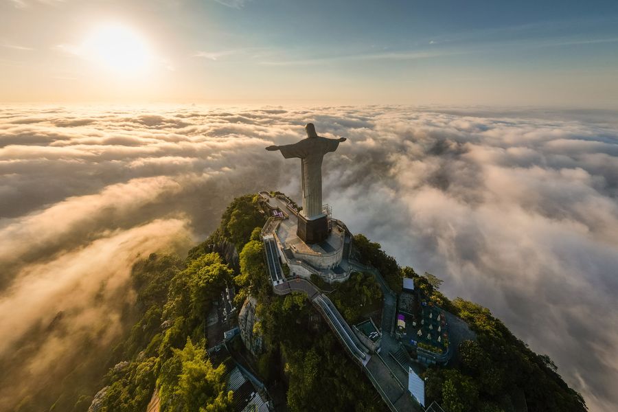 O Cristo Redentor no alto do Corcovado sobre um mar de nuvens ao nascer do sol, visto do alto