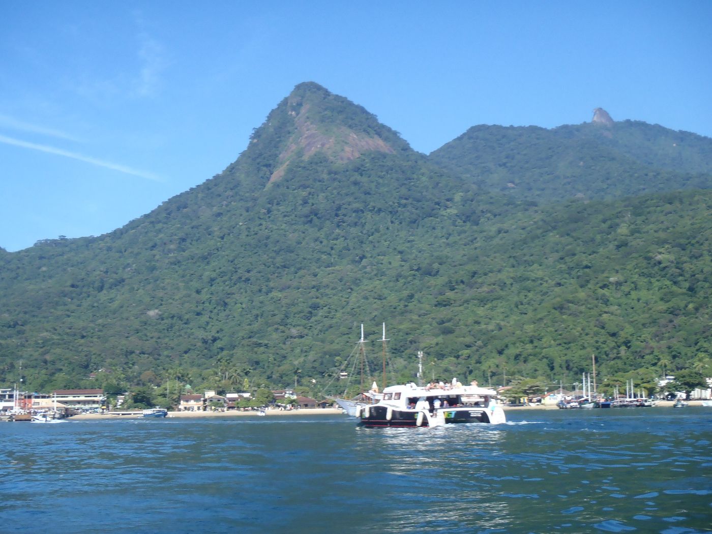 A catamaran ferry off the waterfront of Vila do Abraão, with forested peaks rising behind