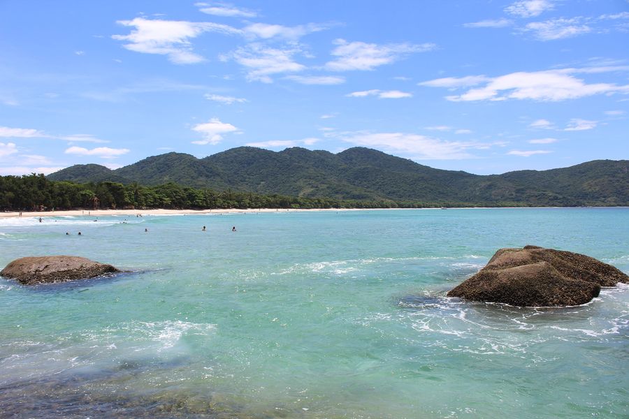 Turquoise water and granite boulders at Lopes Mendes beach on Ilha Grande, with the far end of the beach and green hills in the distance