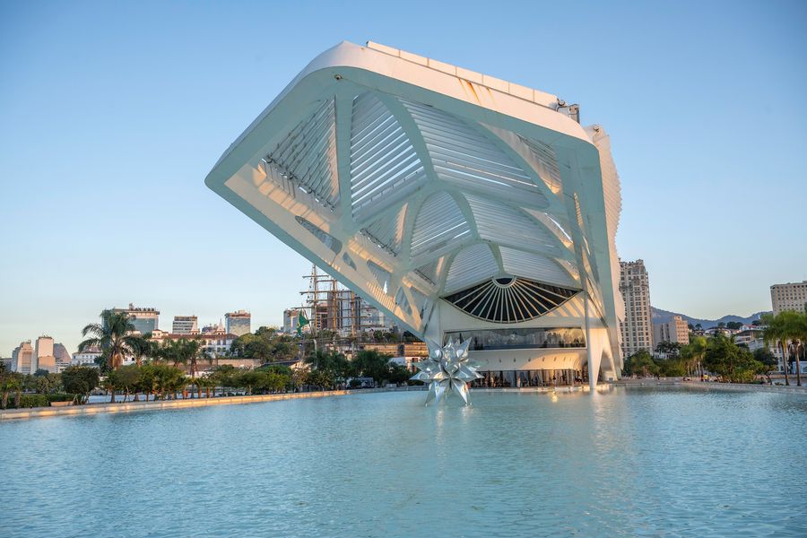 The white, wing-like Museu do Amanhã on the waterfront, reflected in a long pool under a blue sky