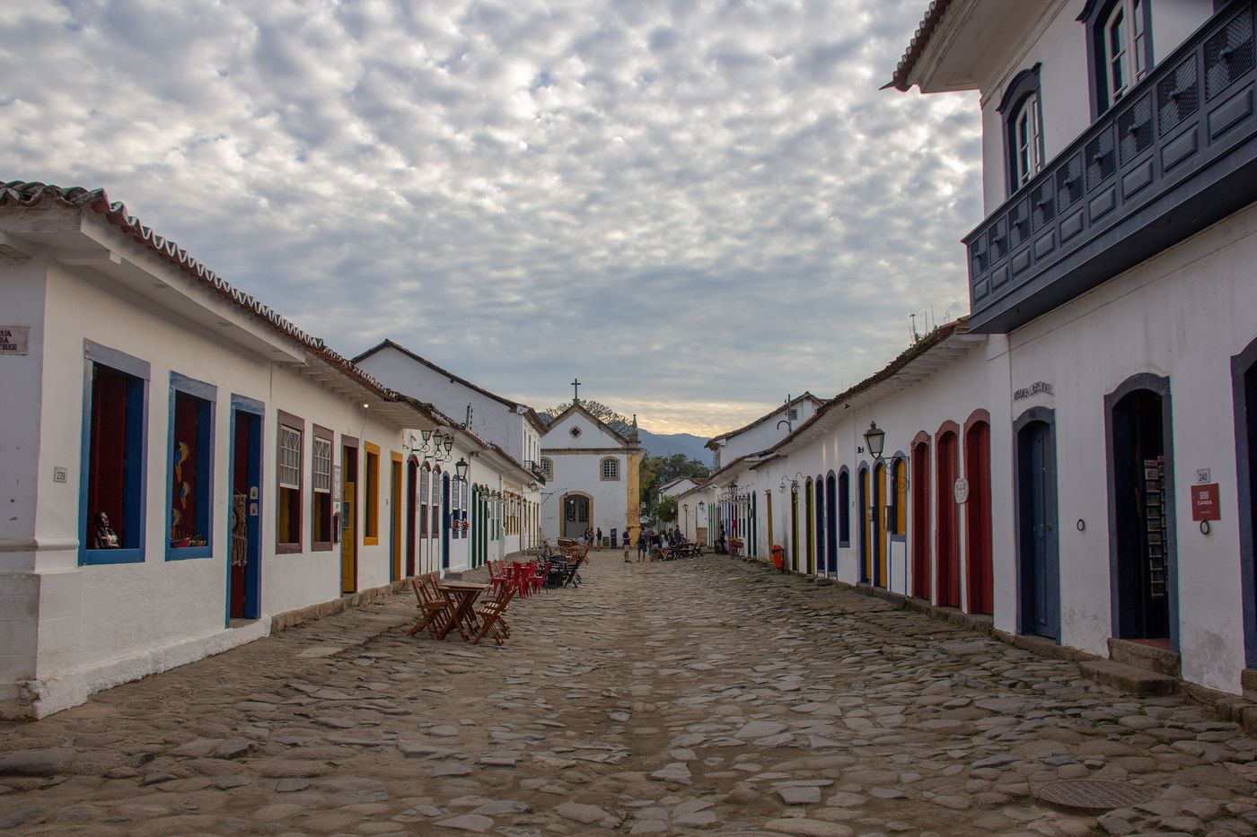 A cobbled street in Paraty lined with whitewashed colonial houses with coloured doors, leading to a small white church