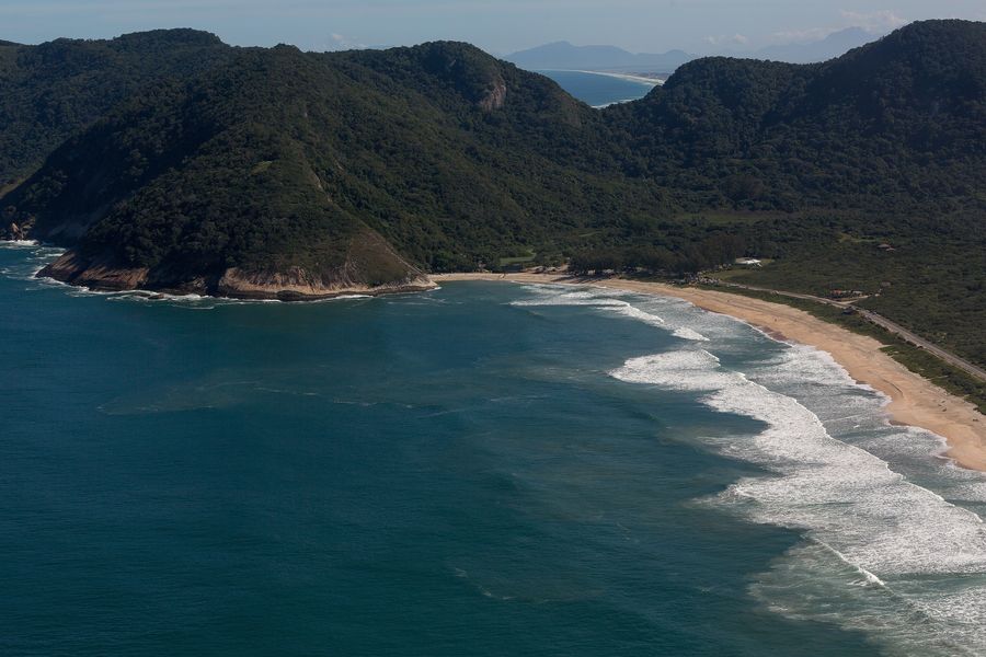 Aerial view of Grumari Beach, a long curve of sand and surf backed by forested hills