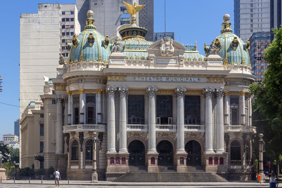 The ornate façade of the Theatro Municipal in central Rio, with green domes and a golden eagle on top, between office towers